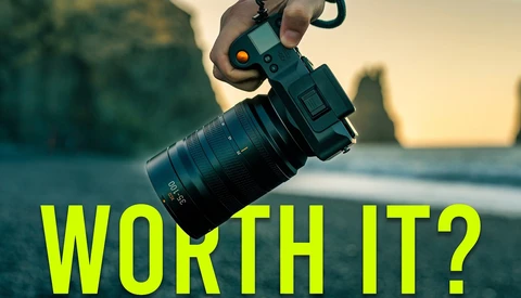 Hand holding a mirrorless camera with telephoto lens against coastal landscape at golden hour