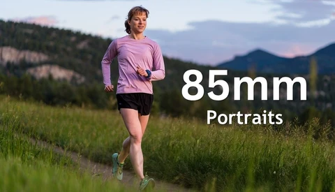 Female runner in purple long-sleeve shirt jogging through grassy meadow with forested mountains in background at dusk