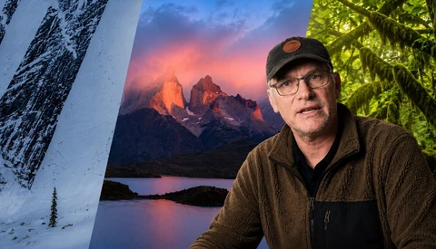 Photographer in glasses and cap positioned in front of landscape photography displays
