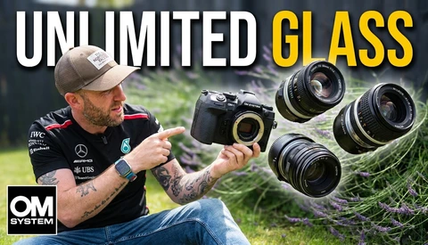 Photographer holding OM System camera with multiple lenses displayed outdoors