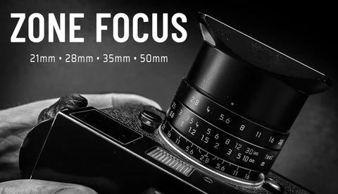 Manual focus lens with zone focus markings mounted on vintage camera body against dark background