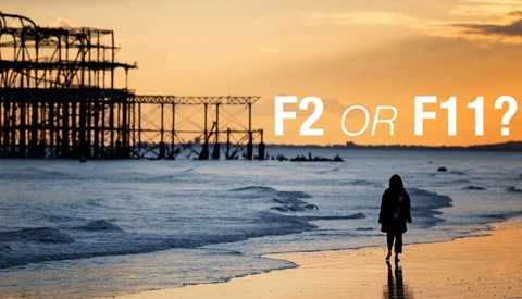 Silhouetted figure wading in ocean at sunset with abandoned pier structure in background