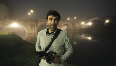 Photographer holding a DSLR camera at night in front of an illuminated stone bridge