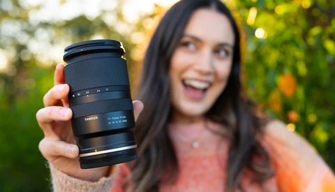 Woman holding a Tamron telephoto lens toward camera in outdoor setting