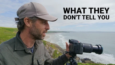Photographer with telephoto lens on tripod overlooking coastal cliffs and ocean waves