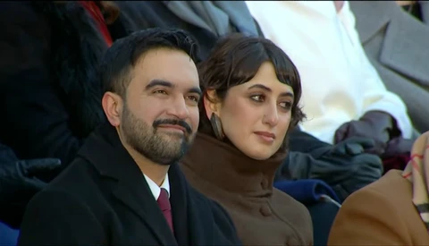 Man and woman sitting together outdoors, dressed in dark winter coats