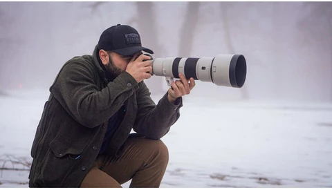 Photographer crouching while composing shot with telephoto lens