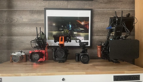 Filmmaker's workspace displaying cameras, lenses, and production gear on wooden desk
