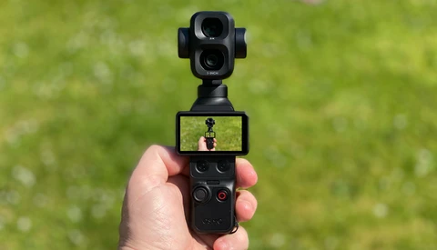 Hand holding DJI Osmo Pocket gimbal camera with articulating screen displaying live preview