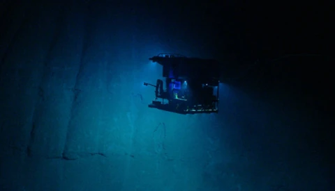 Submersible vessel illuminated by blue lights exploring the deep ocean floor