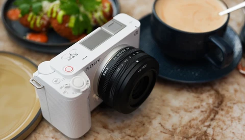 White mirrorless camera with black prime lens on textured surface surrounded by food styling props