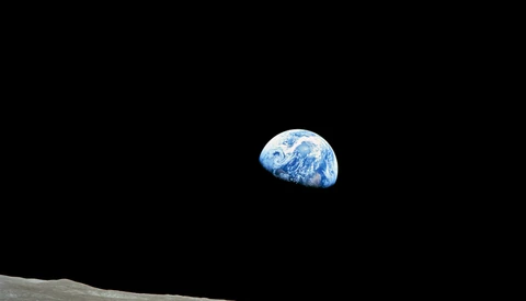 Earth rising above the lunar horizon against black space