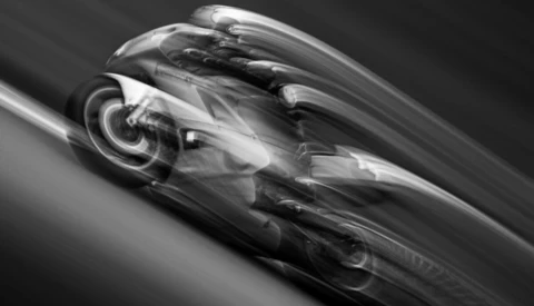 Black and white motion-blurred racing car leaning into a turn on a banked track