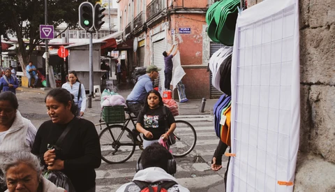 Busy urban street scene with pedestrians and a cyclist among market stalls and storefronts