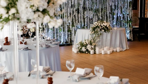 Elegant wedding reception setup with white linens, floral centerpieces, and cascading silver streamer backdrop