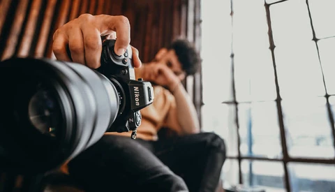 Photographer holding mirrorless camera with telephoto lens, shooting indoors with natural window light
