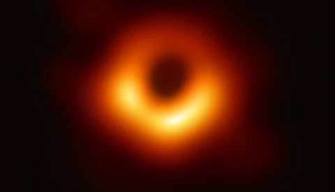 First photograph of a black hole showing bright orange and yellow accretion disk with dark central shadow