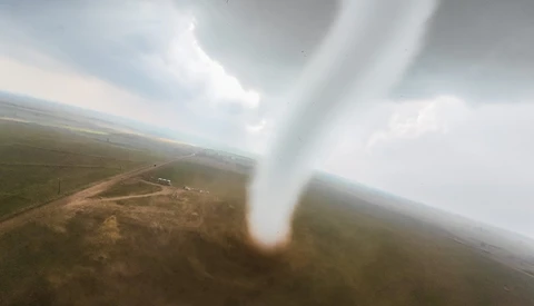 Tornado funnel cloud touching ground in rural landscape viewed from aircraft