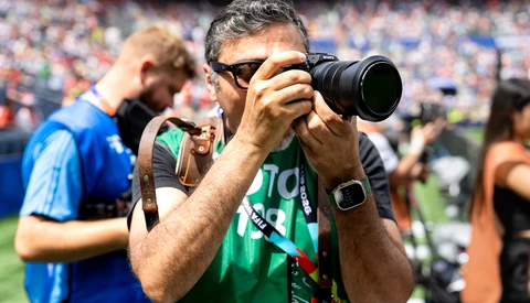 Sports photographer with telephoto lens at stadium event wearing green credential lanyard