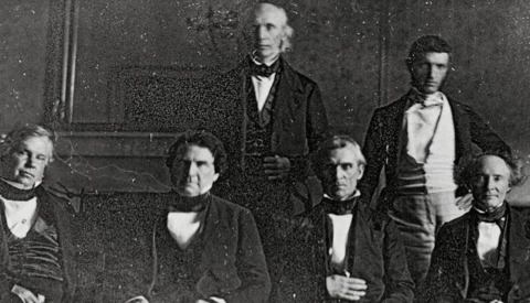 Five men in formal 19th-century attire arranged in a studio portrait