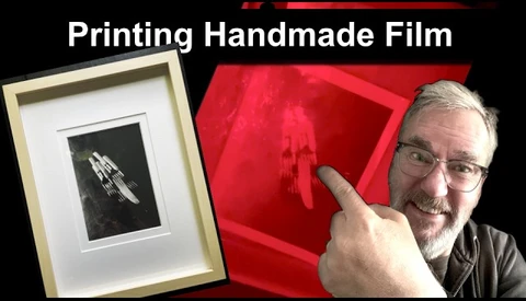 Photographer pointing to framed black and white handmade film print displayed next to red photographic paper
