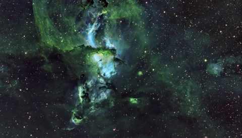 Deep space nebula with green and blue gas clouds surrounding bright stellar formation