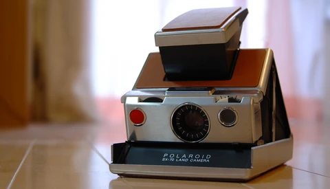 Polaroid SX-70 instant camera with flash attachment stacked on wooden base