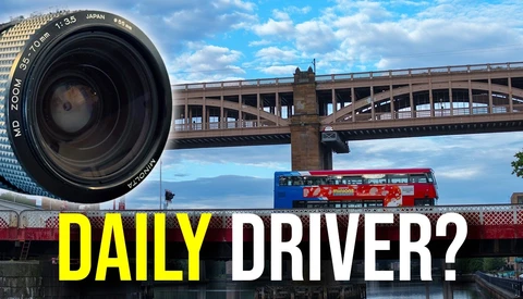Camera lens in foreground with London bridge, red bus, and cityscape in background