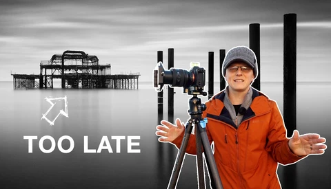 Photographer with camera on tripod wearing orange jacket, with pier structure and text overlay reading "TOO LATE"