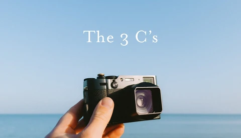 Hand holding a vintage film camera against a clear blue ocean and sky backdrop