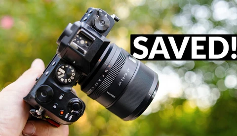 Mirrorless camera with attached lens held in hand against blurred green background