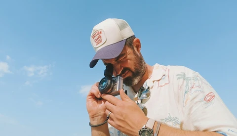 Photographer holding vintage rangefinder camera to eye against clear blue sky