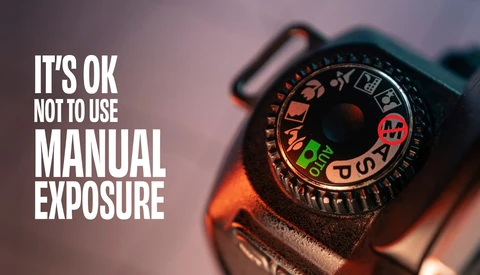 Close-up of a camera's exposure compensation dial with white text overlay reading 'IT'S OK NOT TO USE MANUAL EXPOSURE'
