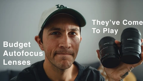Photographer holding two black autofocus lenses while making a skeptical expression