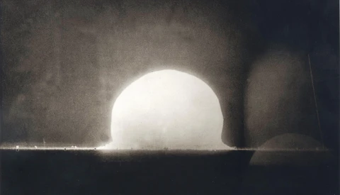 Nuclear explosion test shot showing bright hemispherical fireball rising above desert ground with shock wave and dust plume