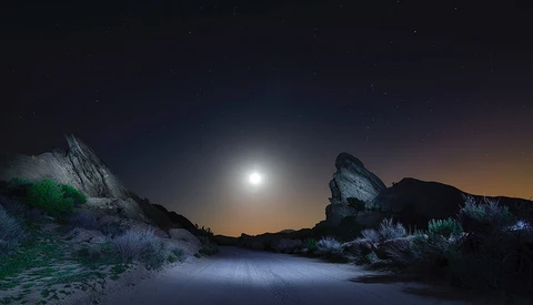 Desert landscape under full moon with illuminated rocky outcrops and sparse vegetation