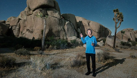 Runner in blue shirt posing in front of large granite boulders under starry night sky