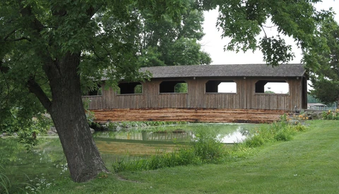 Wooden boathouse with arched openings spanning a calm pond, framed by mature trees