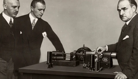 Three men in business suits examine a large industrial machine on a table
