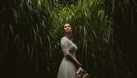 Woman in lace top and flowing skirt standing in tall green corn stalks, looking upward