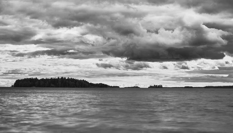 Black and white landscape of forested islands under dramatic storm clouds over calm water
