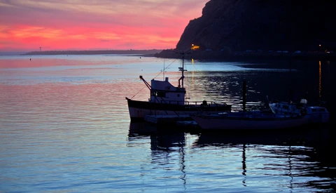 Fishing boat silhouetted at twilight in calm harbor waters with dramatic sunset sky