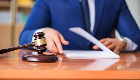 Lawyer in blue suit holding gavel at wooden desk with documents and tablet