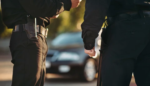 Two people in dark clothing shaking hands at night with blurred vehicles in background