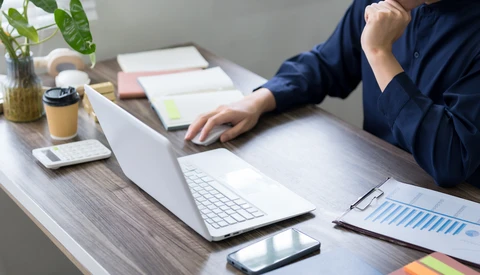 Photographer reviewing work on laptop at desk with smartphone, notes, and coffee