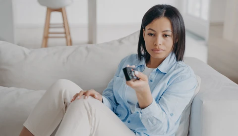 Woman in light blue shirt sitting on gray couch holding remote control