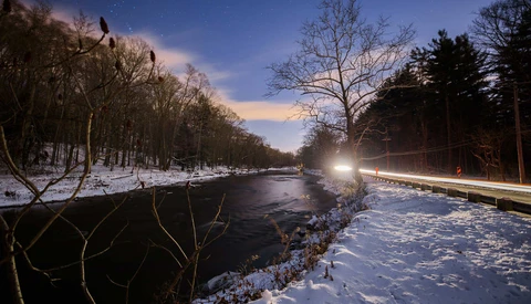 Winter landscape with unfrozen river flowing through snow-covered banks at twilight