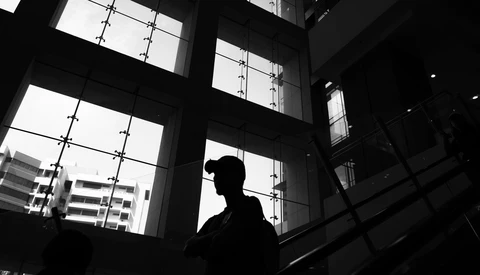 Silhouetted figure against large gridded windows with city buildings visible outside