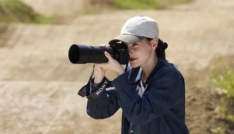 Photographer with camera and telephoto lens wearing cap and navy jacket