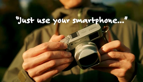 Hands holding a vintage rangefinder camera with overlay text reading "Just use your smartphone..."
